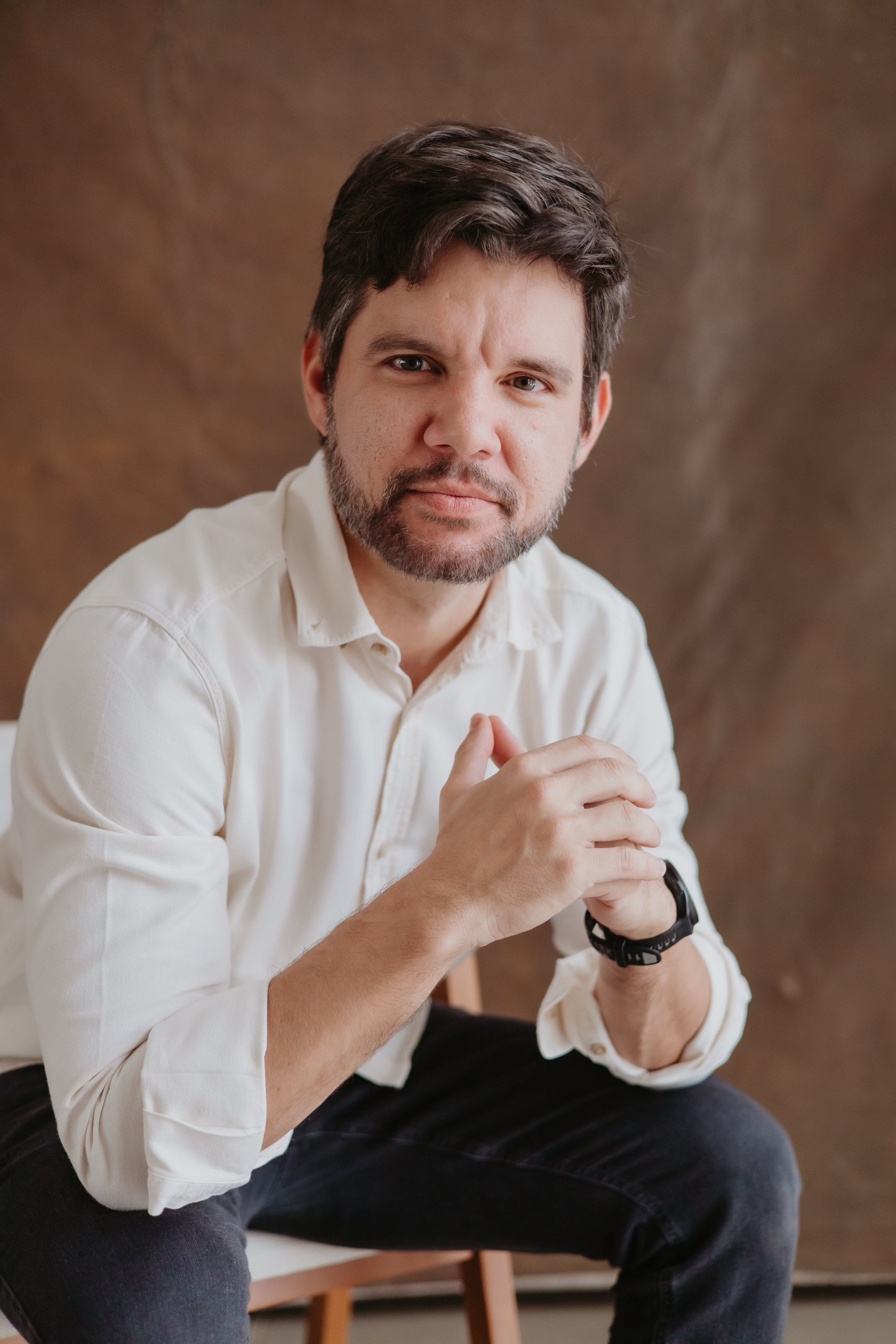 Professor Filipe Miguel, de camisa branca, sentado com as mãos unidas.